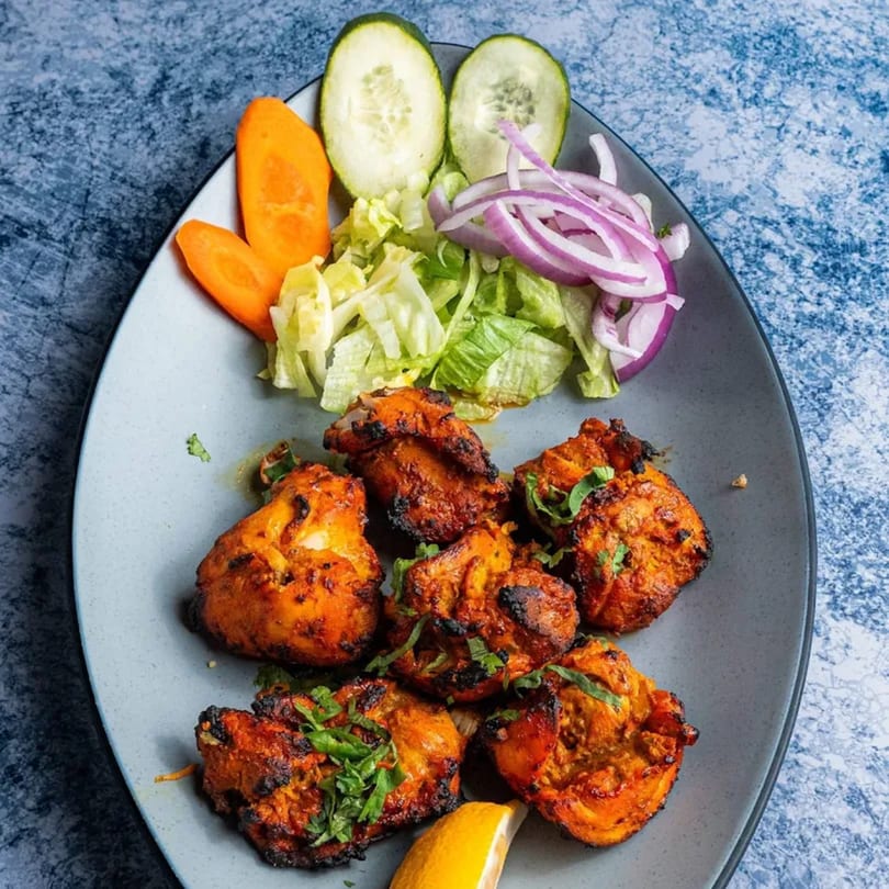 Grilled chicken tikka with fresh salad, sliced cucumbers, carrots, red onions, and a lemon wedge.