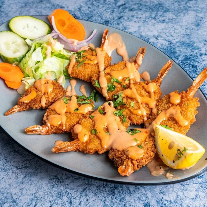 Crispy fried shrimp drizzled with sauce, served with a lemon wedge and a side salad.