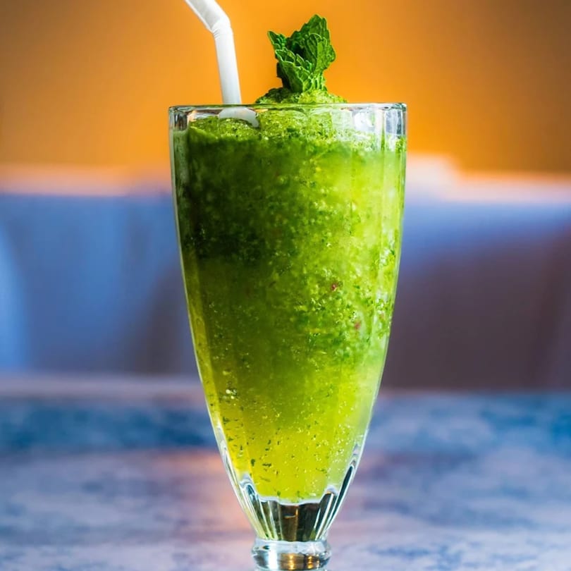 A tall glass of vibrant green mint margarita, garnished with fresh mint leaves and a white straw.