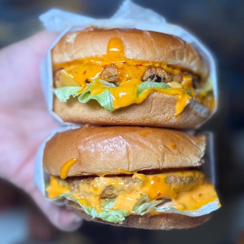 Two stacked halal burgers with melted cheese, lettuce, and sauce, held in a hand.