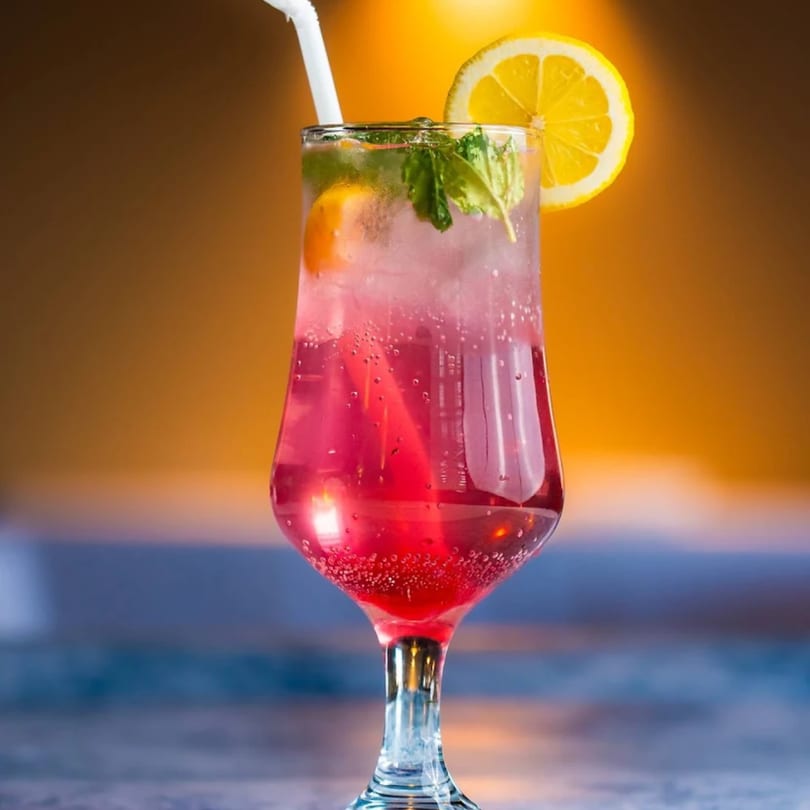 A vibrant red drink with ice, mint, and a lemon slice in a tall glass with a straw.